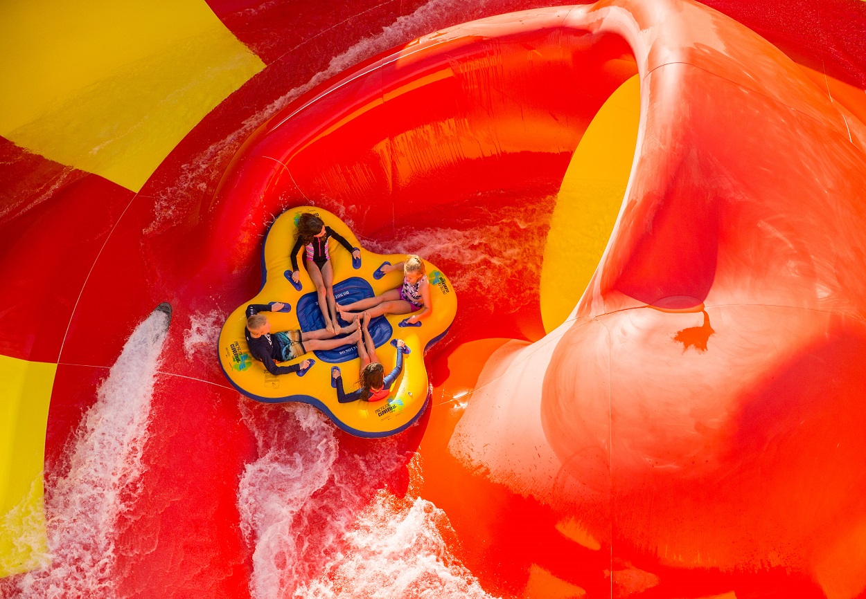 four people on a tube on a red and yellow huge water slide